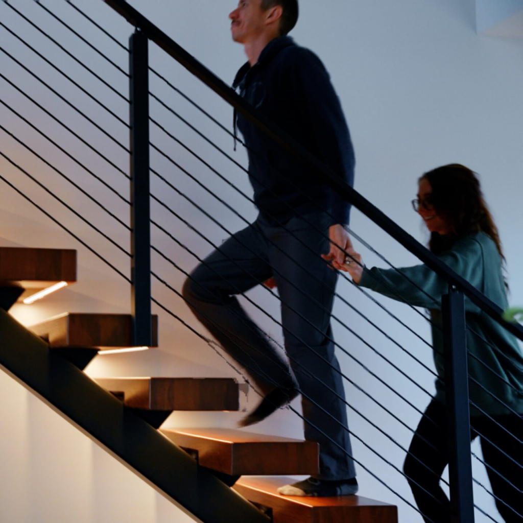 A man and a woman walk up a Viewrail FLIGHT Mono Staircase with LED lights underneath the treads.